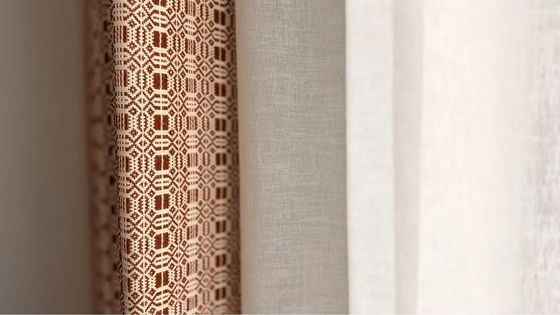 The Giada curtain hanging against plain linen and a sheer, its geometric border woven in rust and cream