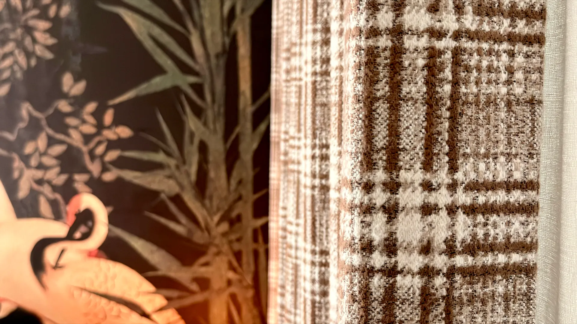 A woven check curtain hanging beside a wall papered with cranes and bamboo