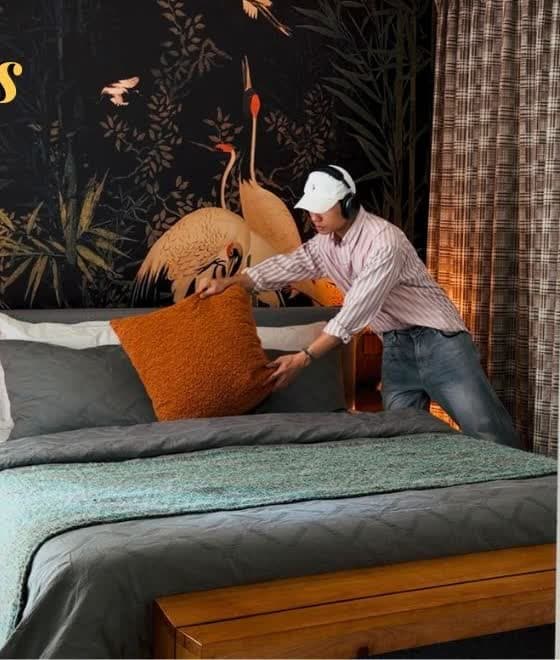 Johannes placing the rust boucle lumbar on the bed under the crane wallpaper