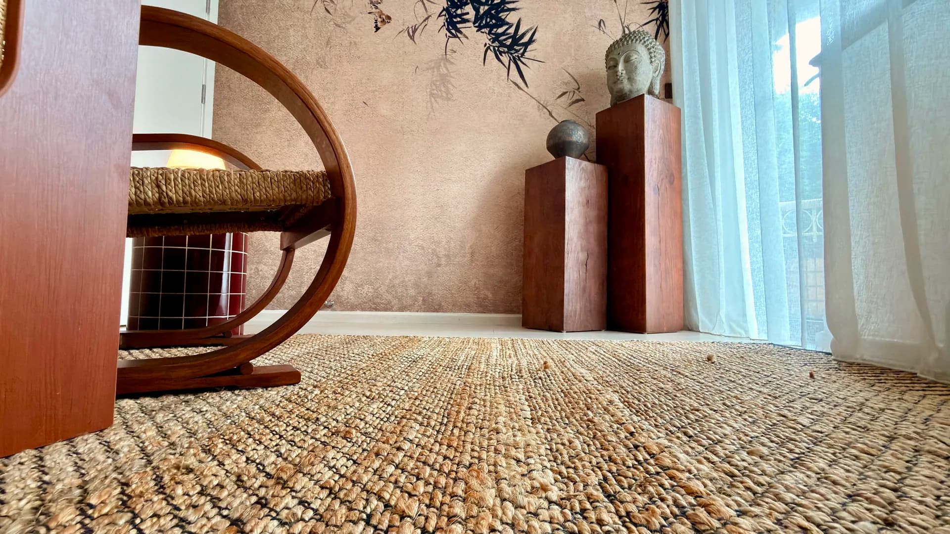 The jute rug running the length of the floor to a pair of wooden plinths and a stone Buddha head