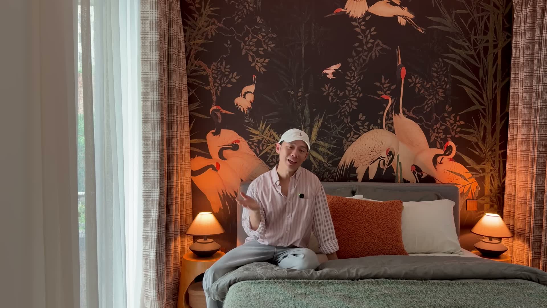 Johannes on his bed in front of the dark crane wallpaper, twin lamps glowing