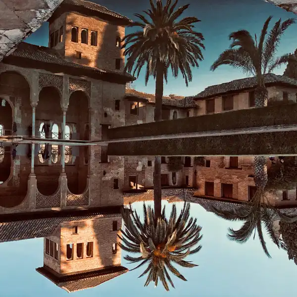 Palm trees and a Spanish courtyard reflected in a pool beneath a blue sky